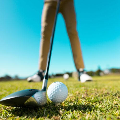 Low section of african american young man aiming golf ball with club against clear sky in summer Low section of african american young man aiming golf ball with club against clear sky in summer